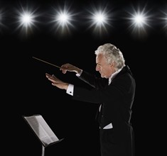 Man in tuxedo conducting under lights. Date : 2008