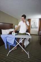 Businessman ironing shirt and talking on cell phone. Date : 2008