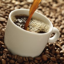 Coffee pouring into mug surrounded by coffee beans. Date : 2008