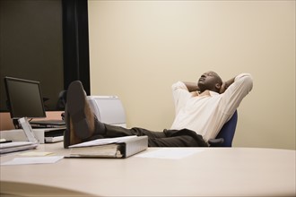 African businessman relaxing with feet on desk. Date : 2008