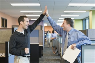 Businessmen high-fiving in office. Date : 2008
