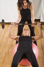 Trainer assisting woman lifting barbell. Date : 2008
