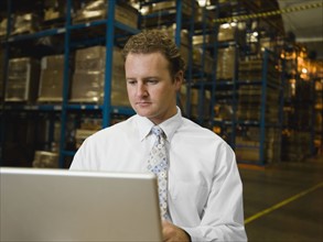 Businessman looking at laptop in warehouse. Date : 2008