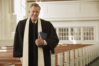 Priest standing next to pews. Date : 2008