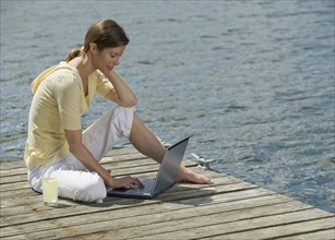 Woman using laptop on dock.