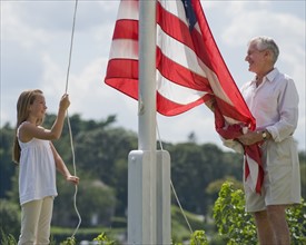 Grandfather and granddaughter raising American flag.