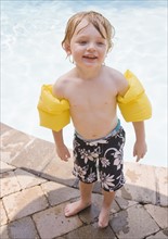 Preschool boy with inflatable arm bands standing poolside. Date : 2008