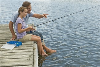 Father and daughter fishing off dock.