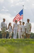Multi-generational family walking in front of American flag.