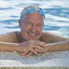 Senior man resting on edge of swimming pool.