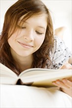 Teenage girl reading book on bed. Date : 2008