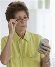 Senior woman reading label on food can.