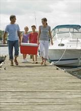 Family walking on boat dock with cooler.