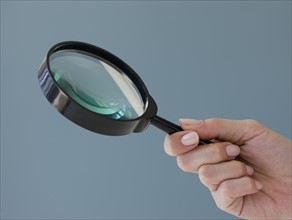 Close up of hand holding magnifying glass.
