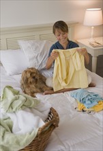 Girl folding clothes on bed.