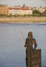 Statue in front of river and city.