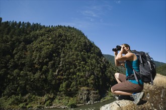 Hiker looking through binoculars on river overlook. Date : 2008