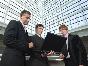 Businessmen looking at laptop in convention center atrium. Date : 2008