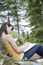 Girl leaning against tree writing in notebook. Date : 2008