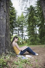 Girl leaning against tree writing in notebook. Date : 2008