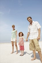 Girl holding hands with mother and father on beach. Date : 2008