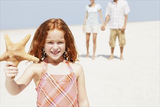 Girl holding up starfish on beach. Date : 2008