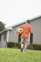 Boy carrying soccer ball in backyard. Date : 2008