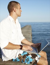 Young man using laptop on dock. Date : 2008