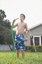 Boy drinking from garden hose in backyard. Date : 2008