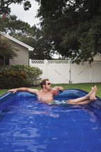 Man relaxing in inflatable swimming pool. Date : 2008