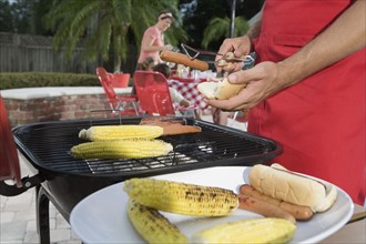 Man grilling hotdogs and corn in backyard. Date : 2008