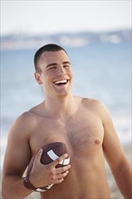 Young man holding football on beach. Date : 2008
