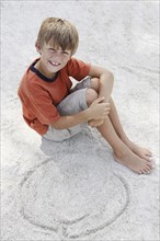 Boy drawing designs in beach sand. Date : 2008