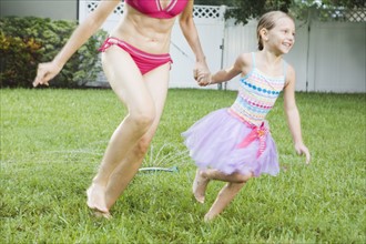 Mother and daughter running through sprinkler. Date : 2008