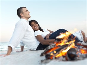Young couple relaxing by campfire on beach. Date : 2008