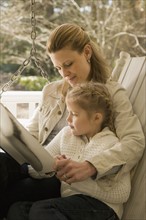 Mother reading to daughter on porch swing. Date : 2008