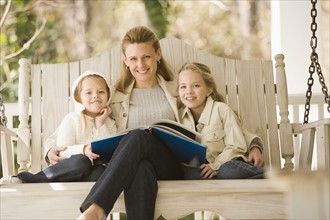 Mother reading to daughters on porch swing. Date : 2008