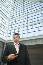 Businessman looking at cell phone in convention center atrium. Date : 2008