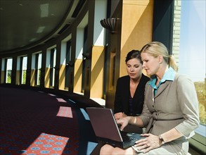 Businesswomen looking at laptop in office corridor. Date : 2008