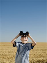 Boy in field looking through binoculars . Date : 2008