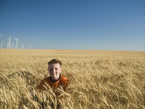 Boy sitting in tall wheat field on wind farm. Date : 2008