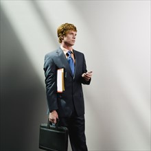 Businessman holding cell phone, files and briefcase. Date : 2008