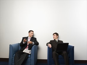 Businessmen sitting in chairs in office lobby. Date : 2008