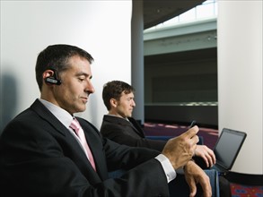 Businessmen sitting in chairs in office lobby. Date : 2008