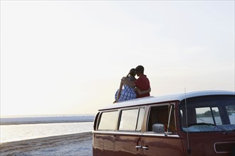 Couple watching ocean sunset from top of van. Date : 2008