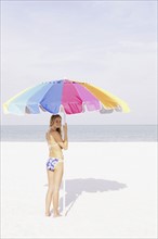 Teenage girl holding umbrella on beach. Date : 2008