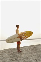 Teenage boy holding surfboard on beach. Date : 2008