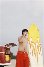 Teenage boy holding surfboard on beach. Date : 2008