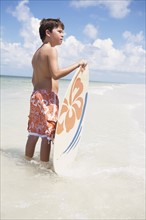 Boy holding skimboard in ocean. Date : 2008