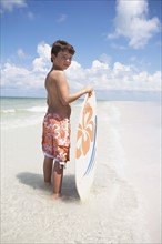 Boy holding skimboard in ocean. Date : 2008